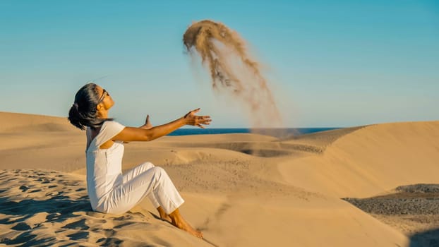 woman at the beach of Maspalomas Gran Canaria Spain, a girl at the sand dunes desert of Maspalomas Spain Europe throwing sand in the air