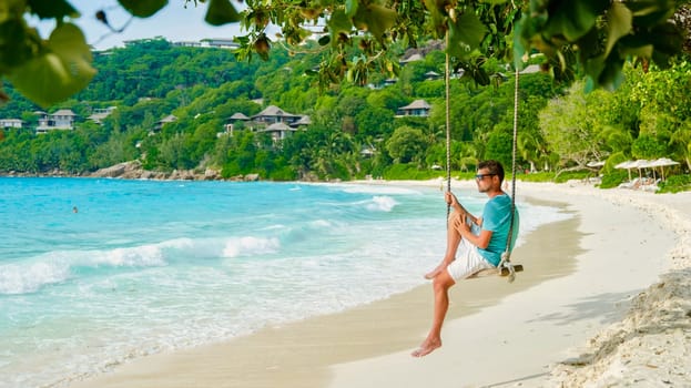 Young men relaxing in a swing on the beach of Mahe Tropical Seychelles Islands. man on a luxury vacation at the Seychelles