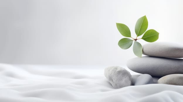 A stack of smooth grey stones with a green plant on a white fabric. This image creates a sense of balance and harmony. The stones are of different sizes and are arranged in a vertical order. High quality photo
