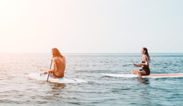 Woman man sup yoga. Happy young sporty couple practising yoga pilates on paddle sup surfboard. Female stretching doing workout on sea water. Modern family outdoor summer sport activity