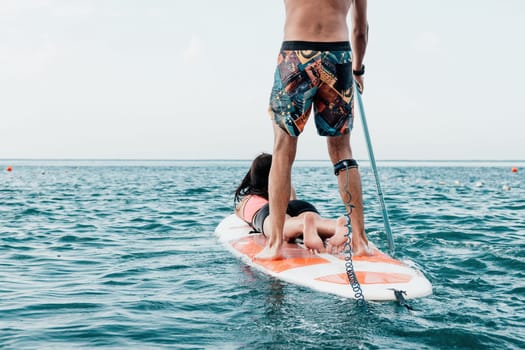 Sea woman and man on sup. Silhouette of happy young woman and man, surfing on SUP board, confident paddling through water surface. Idyllic sunset. Active lifestyle at sea or river