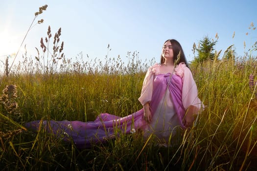 Young plump curvy beautiful teenage girl in a field or meadow on sunny summer day in the evening sunset sun. Plump black-haired and black-eyed oriental model from the east fairy tale