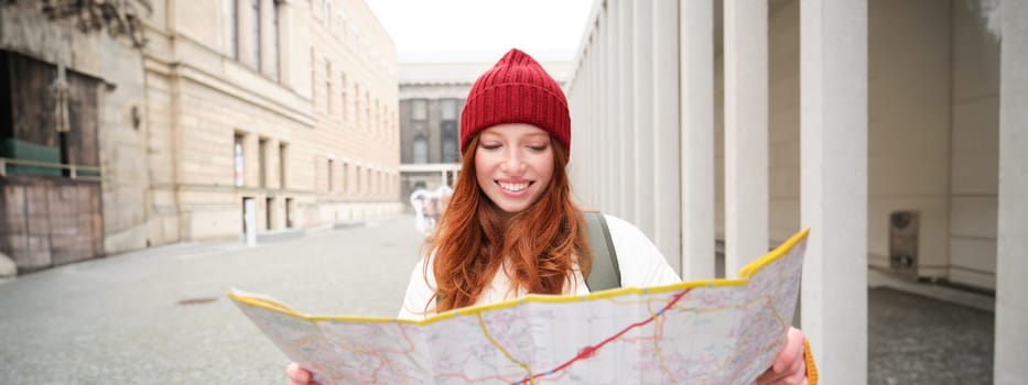 Redhead girl, tourist explores city, looks at paper map to find way for historical landmarks, woman on her trip around euope searches for sightseeing.