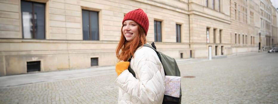 Tourism and travelling. Young redhead woman smiling, tourist walking with backpack around city centre, sightseeing, holds backpack with paper map.
