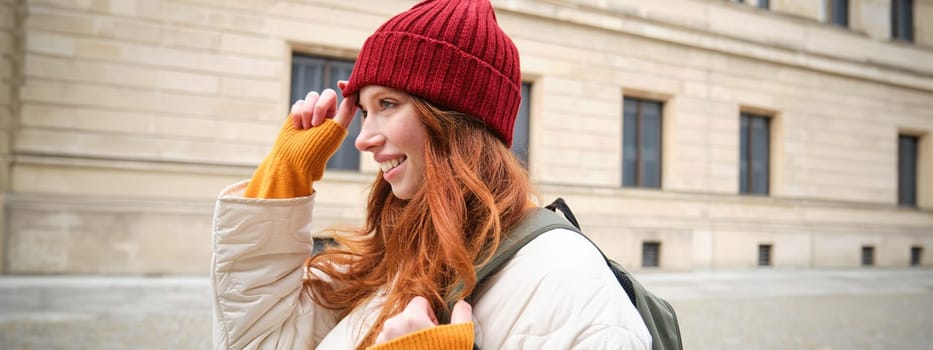 Tourism and travelling. Young redhead woman smiling, tourist walking with backpack around city centre, sightseeing, holds backpack with paper map.