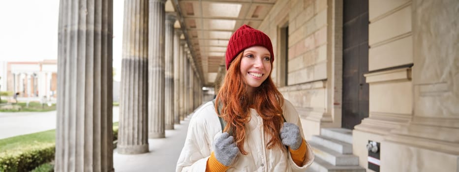 Happy girl traveller with red long hair, walking in city, sightseeing, backpacking around europe in winter.