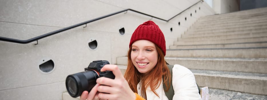 Urban people and lifestyle. Happy redhead woman takes photos, holding professional digital camera, photographing on streets.