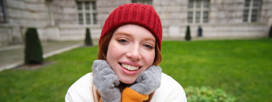 Cute girl student in red hat, warm gloves, sits in park, smiles and looks happy. Copy space