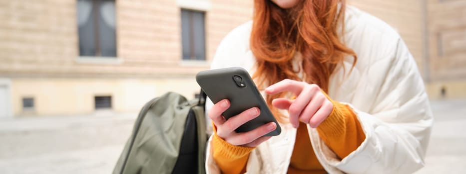 Close up of female hands typing on mobile phone, using smartphone app. GIrl with telephone types, sits outdoors and uses map.