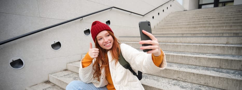 Urban girl takes selfie on street stairs, uses smartphone app to take photo of herself, poses for social media application.