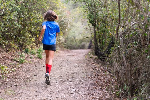 rear view of a kid practicing trail running in the forest, concept of sport in nature and healthy lifestyle for children, copy space for text