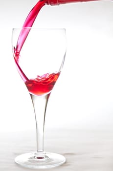 Filling a crystal glass with red cherry liquer, drink, on white background