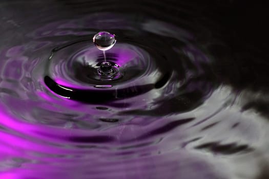 A drop splashes in water with shade of pink