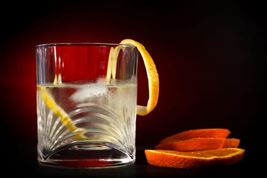 Cold vodka in a glass, with decor oranges and lemon, in black red background, part of art beverage background