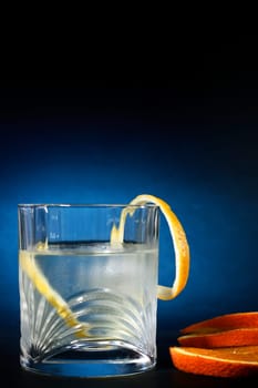 Cold vodka in a glass, with decor oranges and lemon, in black blue background, part of art beverage background