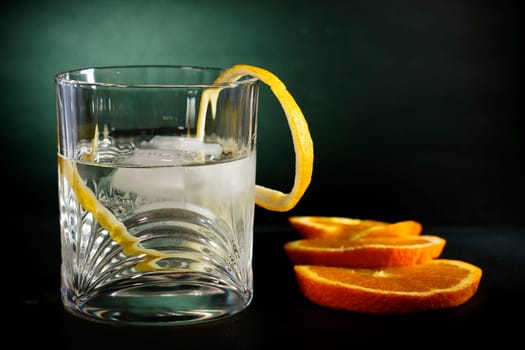Cold vodka in a glass, with decor oranges and lemon, in black green background, part of art beverage background