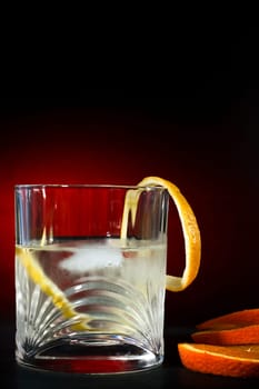 Cold vodka in a glass, with decor oranges and lemon, in black red background, part of art beverage background