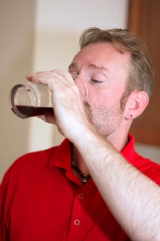 Middle aged man with his arm raised drinking a dark purple fruit juice out of a tall clear beverage glass.