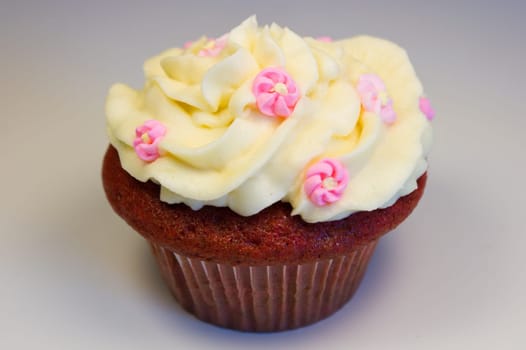 Red velvet cupcake with buttercream icing with flower decorations isolated on white.