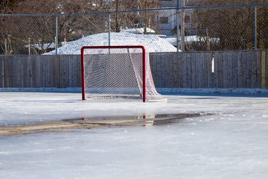 Ice hockey rink with hockey net on melting ice in the early spring.