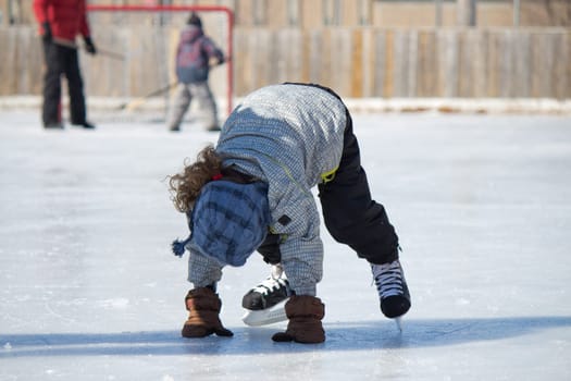 Child playing and skating at the outdoor skating rink in winter.