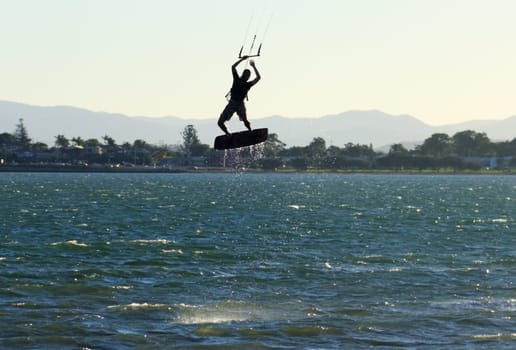 Kite surfer airborne above the water at sunset.