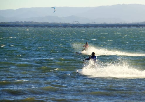Two kite surfers speeding along the water at sunset.