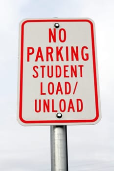 Red and white metal sign at a public school that reads in all capital letters, no parking student load / unload.