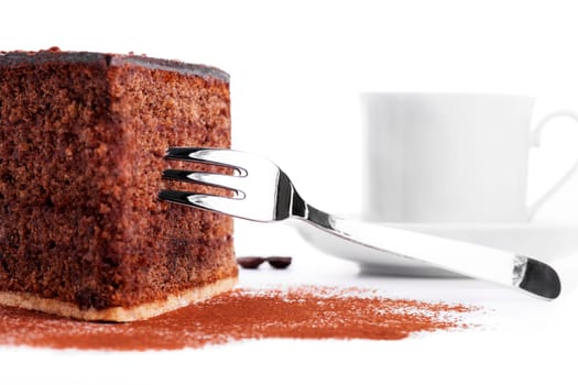Chocolate cake with fork in front of a cup of coffee on a white background