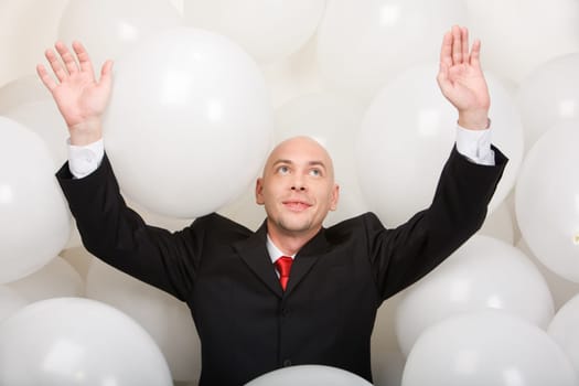 Photo of joyful man wearing suit inside balloons raising his arms