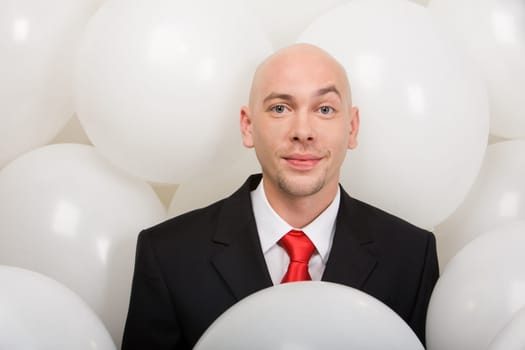 Handsome businessman surrounded by many balloons looking at camera with smile
