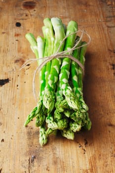 Bunch of fresh green asparagus spears tied with string on a rustic wooden table top