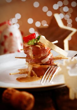 Festive Banquet Meal. Delicious Menu served on a white plate. Tenderloin staple wrapped in bacon with a yummy sauce. Christmas decoration in the background