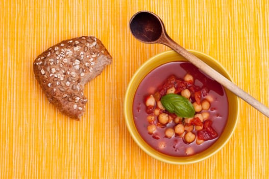 Red soup with chickpeas,tomatoes and basil and wooden spoon