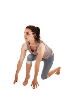 A young skinny woman is in start up position in the studio in bare feet and blue thighs for white background.
