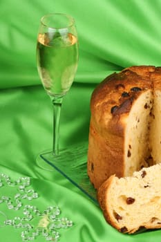 Panettone the italian Christmas fruit cake served on a transparent glass plate a glass of spumante and some ornaments over a green background. Selective focus.