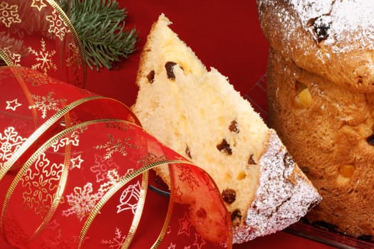 Panettone the italian Christmas fruit cake served on a transparent glass plate with a red and golden ribbon over a red background. Selective focus.