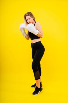 Woman boxer in gloves training on a yellow and dark studio background