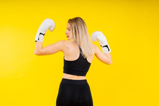 Woman boxer in gloves training on a yellow and dark studio background