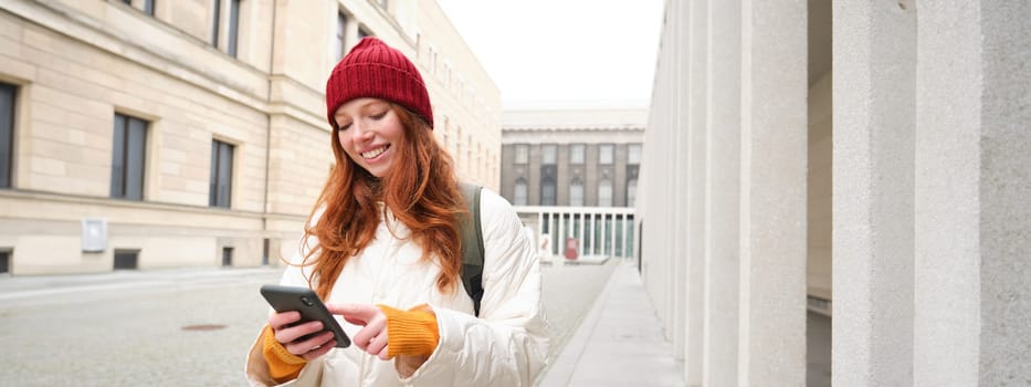 Tourism and technology. Beautiful redhead girl tourist, looking for a route on application, using city map on smartphone, reading about sightseeing places on mobile phone.