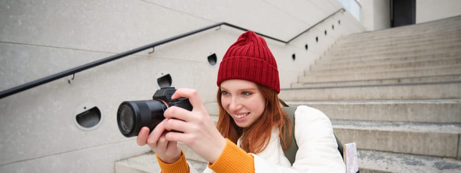 Urban people and lifestyle. Happy redhead woman takes photos, holding professional digital camera, photographing on streets.