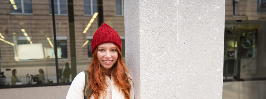 Beautiful redhead girl with smartphone, standing on street, holding mobile phone, using taxi app, connects to public wifi and uses internet, sends a text message.