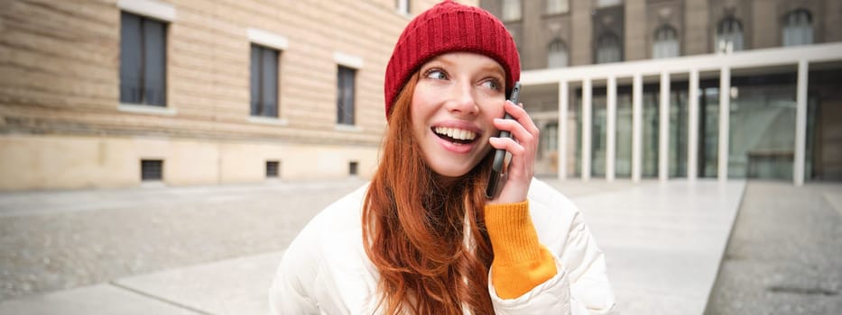 Mobile connection and people concept. Happy redhead woman in hat, talks on mobile phone, making telephone call, using app to call abroad.