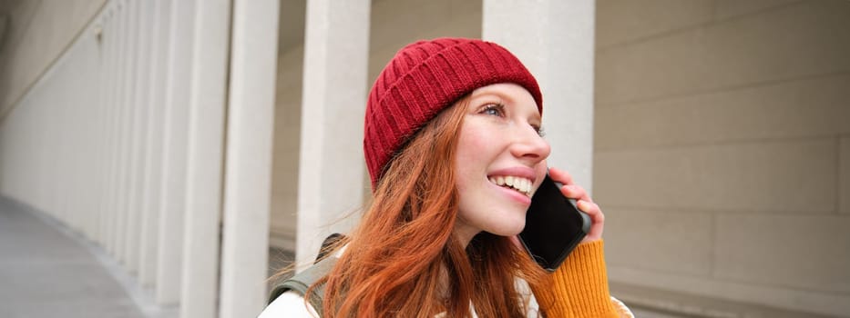 Happy redhead woman, girl with phone talks, has conversation on mobile app, uses internet to call abroad with smartphone app, laughing and smiling.