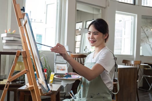 close up picture of happy young Asian woman painting brush on canvas in painting studio. In the art workshop class..