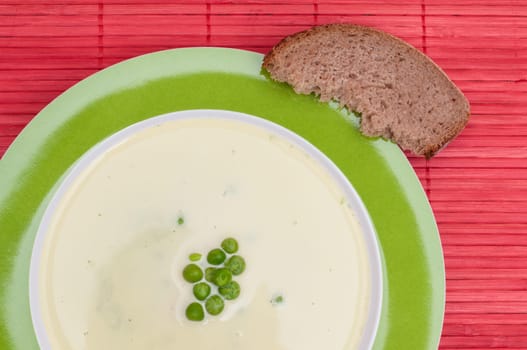 Pea soup with a slice of bread on red bamboo tablecloth