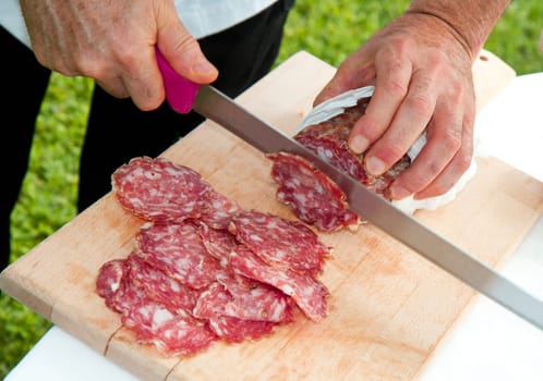 Hand closeup cuts salami with slice pieces at table