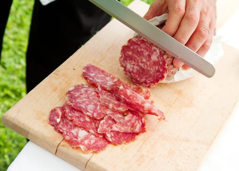 Hand closeup cuts salami with slice pieces at table