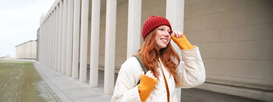 Female tourist in red hat with backpack, sightseeing, explores historical landmarks on her trip around europe, smiling and posing on street.