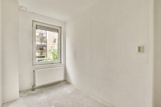 an empty room with white walls and no one person standing in the corner looking out at the view from the window